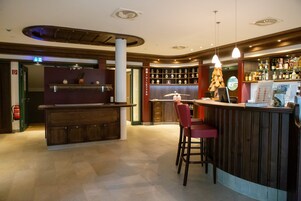 A bar area with a counter, stools, and a shelf with bottles.