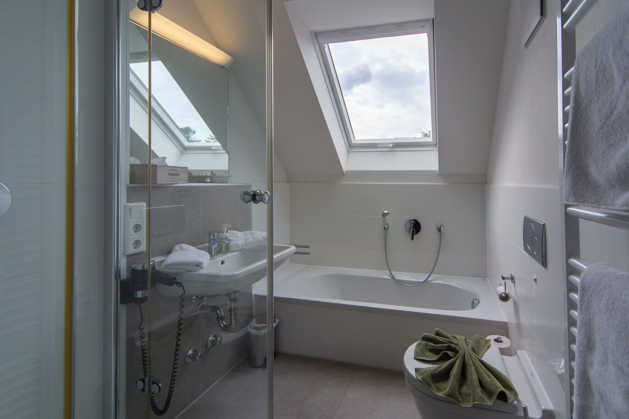 A modern bathroom with a glass-enclosed shower, a freestanding bathtub, and a skylight.