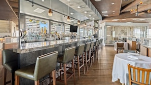 Eine moderne Bar mit einer langen Theke, mehreren Barhocker und einem Fernsehbildschirm.
