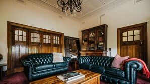 A living room with two dark leather sofas, a wooden coffee table with a book, and a wooden cabinet with glass doors. - Green Gables King Suite (Castlemaine)