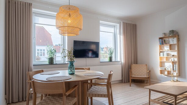 A modern living room with a wooden dining table, chairs, a TV, and a bookshelf. - Apartment Sleeps 2 With Free Parking (Aalborg)