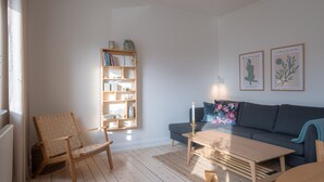 A living room with a wooden bookshelf, a dark grey sofa, a wooden coffee table, and a wicker chair. - Apartment Sleeps 2 With Free Parking (Aalborg)