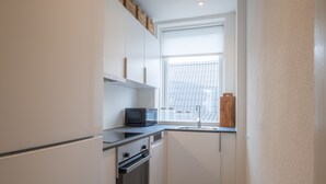 A compact kitchen with white cabinets, a built-in oven, a microwave, and a window with blinds. - Apartment Sleeps 2 With Free Parking (Aalborg)
