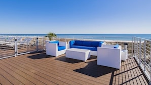 A deck with white wicker furniture and a view of the beach.