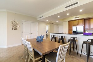 Uma cozinha espaçosa com armários de madeira, uma ilha central com banquetas e uma área de jantar com uma mesa grande e cadeiras.