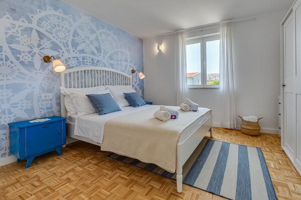 Une chambre à coucher avec un lit, une table de chevet, une fenêtre et un mur décoré d’un motif.