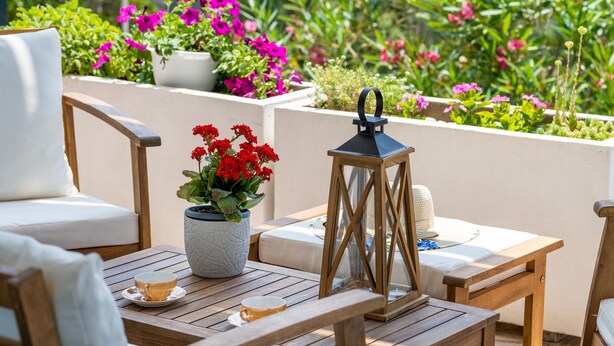 A patio with wooden furniture, a white cushioned chair, a table with a cup and saucer, a potted plant with red flowers, and a lantern. - Family Villa  Pag  2 min from the beach hot tub  - free parking (Pag)