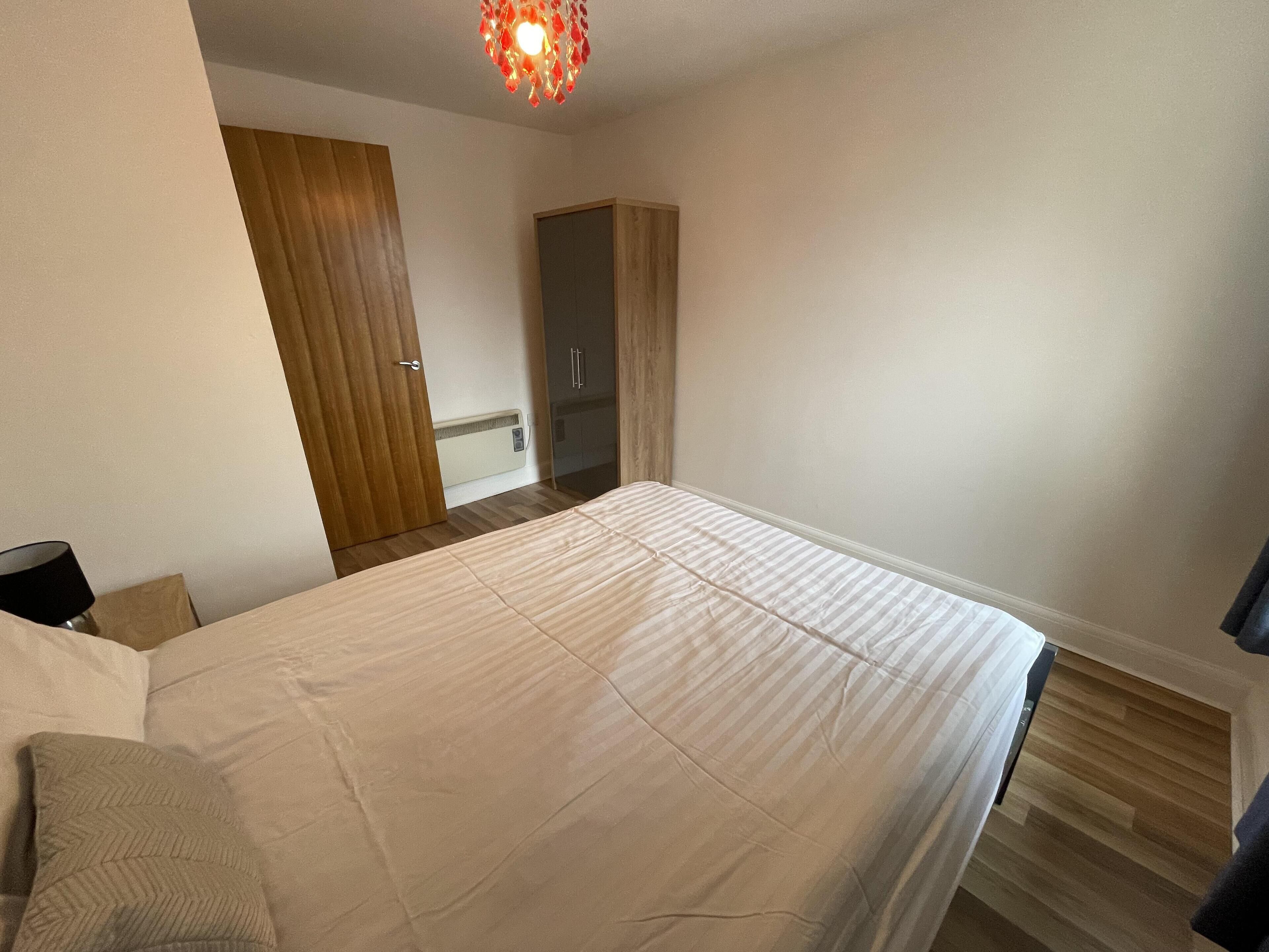 A bedroom with a bed, a wooden wardrobe, a mirror, and a ceiling light fixture.