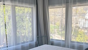 Quarto com cama, janela com cortinas leves e um respiradouro no teto.