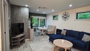 Uma sala de estar moderna com televisão, sofá, mesa de centro e uma área de jantar com cadeiras e mesa.