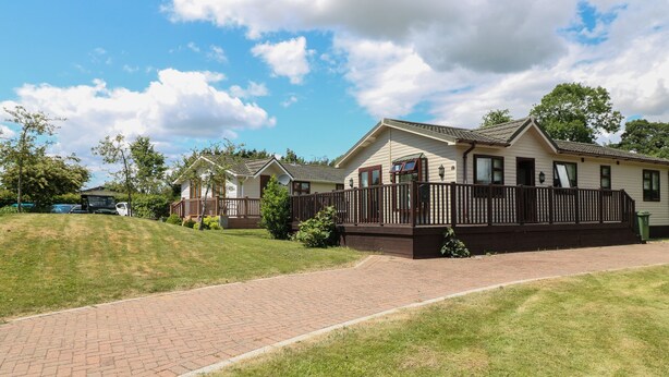 A row of single-story cabins with a brick pathway leading to the entrance. - 27 Brocklehurst (Oakham)