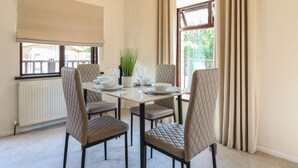 A dining room with a table set for four, four cushioned chairs, a potted plant, and a window with curtains. - 27 Brocklehurst (Oakham)
