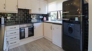 A modern kitchen with white cabinets, a black refrigerator, a dishwasher, and a window with a view of greenery. - 27 Brocklehurst (Oakham)