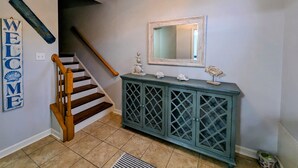 A staircase with a wooden handrail leading to a landing. A cabinet with decorative items and a mirror is on the landing.