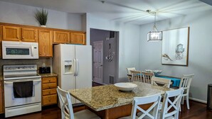 A kitchen with wooden cabinets, a white refrigerator, a microwave, an oven, and a dining area with a table and chairs.
