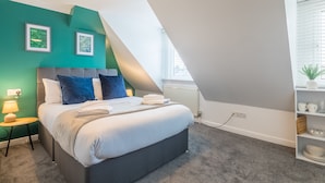 A modern bedroom with a bed, a nightstand, a lamp, and a shelf with decorative items.
