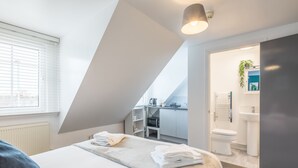 A modern bedroom with a large bed, a built-in desk, and a view of the city through the window.