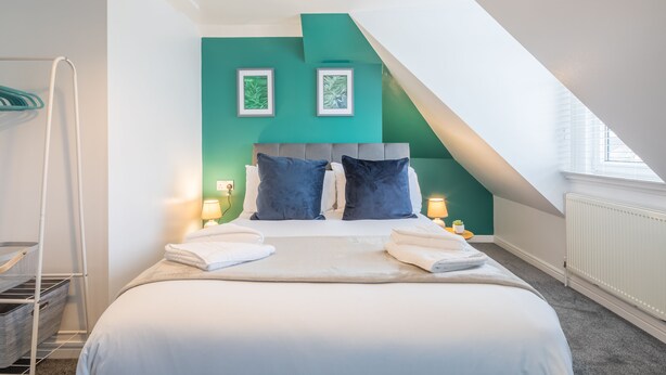 A modern bedroom with a bed, pillows, and a nightstand with a lamp.