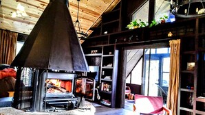 A cozy living room with a large fireplace, wooden beams on the ceiling, and a bookshelf filled with books and decorative items. - Enjoy A memorable experience in our unique Cabin on Wisconsin River (Mauston)