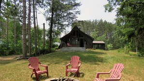 A cabin with a fire pit and three Adirondack chairs in a forested area. - Enjoy A memorable experience in our unique Cabin on Wisconsin River (Mauston)