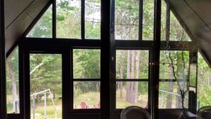 A room with large windows offering views of a forested area, a wicker chair, and a potted plant. - Enjoy A memorable experience in our unique Cabin on Wisconsin River (Mauston)