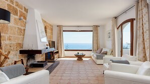 A living room with a stone wall, a fireplace, a sofa, and a view of the sea.