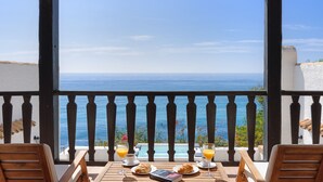 A balcony with a view of the sea, a table with breakfast items, and two chairs.