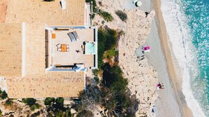 An aerial view of a beachside property with a tiled roof, a swimming pool, and a patio area.
