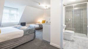 A modern hotel room with two beds, a shower, and a small kitchenette.