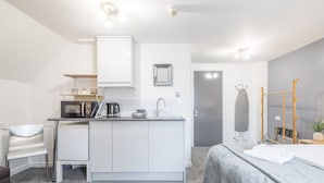 A compact, modern room with a kitchenette, a bed, a desk, and a chair.