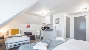 A modern hotel room with two beds, a kitchenette, a desk, and a bathroom.