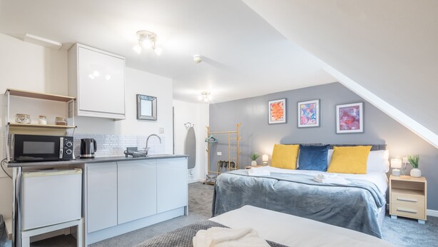 A modern bedroom with a bed, bedside table, and a small desk area with a microwave and kettle.