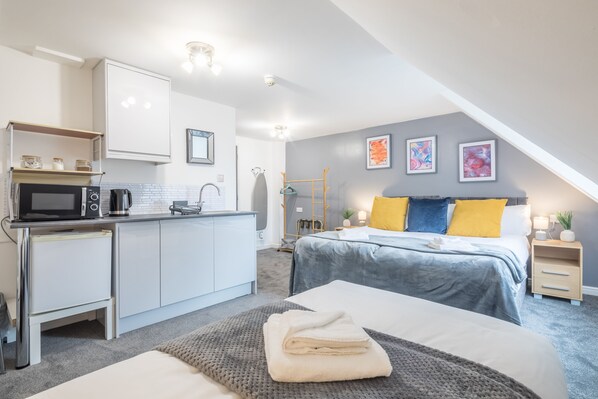 Cozy retreat with a kitchenette, microwave, kettle, and coffee maker. The room features a comfortable bed with a bedside table, lamp, and a small plant.