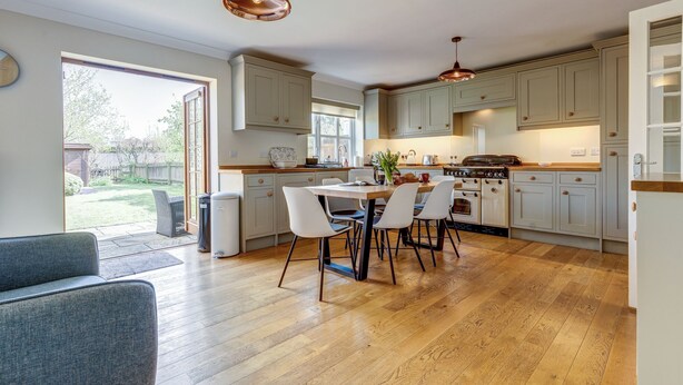 A modern kitchen with wooden flooring, a dining table with chairs, and a large window. - Walnut Cottage | Evenley Holiday Let | 2 Beds & Sleeps 4 (EVENLEY, NEAR BICESTER)