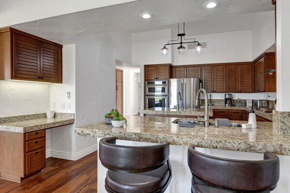 A modern kitchen with wooden cabinets, stainless steel appliances, granite countertops, and a bar area with stools. - Sensational 3 Bedroom 3.5 Bath Private Pool Home With Stunning Views (La Quinta)