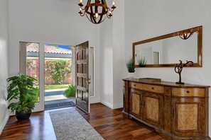 Un couloir avec un plancher en bois, un grand miroir, un meuble en bois et une plante en pot.