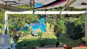 A covered outdoor area with a colorful mural on the wall, a small garden, and a white chair. - Maison Entre lac et Mer, Avec Jardin Ombragé (Villeneuve-de-la-Raho)