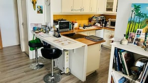A compact kitchen with white cabinets, a wooden countertop, a built-in oven, and a small island with stools. - Maison Entre lac et Mer, Avec Jardin Ombragé (Villeneuve-de-la-Raho)