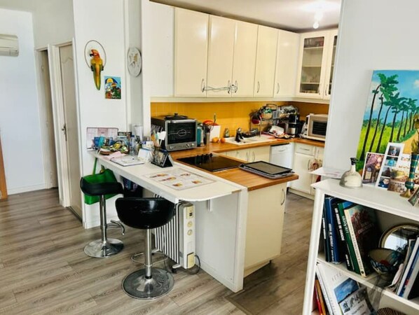 Eine kompakte Küche mit weißen Schränken, einer Holzarbeitsplatte, einem eingebauten Backofen und einer kleinen Kochinsel mit Hockern.