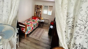 A small, cozy bedroom with a single bed, a wooden bookshelf, a desk with a chair, and a window with blinds. - Maison Entre lac et Mer, Avec Jardin Ombragé (Villeneuve-de-la-Raho)