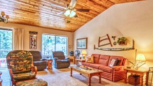 Una sala de estar acogedora con un alto techo de madera, un sofá a cuadros y dos sillones.