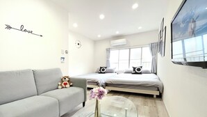 A modern, well-lit room with a grey sofa, a glass coffee table, a bed with two pillows, and a TV mounted on the wall. - 【大阪No.1ロケーション】JR大阪駅、人気の梅田エリアから徒歩圏内。大阪観光地、USJ、難波、京都へ好アクセス！ (大阪市北区中津)