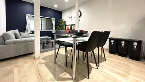 A modern living room with a grey sofa, a glass dining table with black chairs, and a dark blue accent wall. - 【大阪No.1ロケーション】JR大阪駅、人気の梅田エリアから徒歩圏内。大阪観光地、USJ、難波、京都へ好アクセス！ (大阪市北区中津)