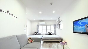 A modern, well-lit room with a sofa, a bed, a glass coffee table, and a TV displaying a beach scene. - 【大阪No.1ロケーショ ン】JR大阪駅、人気の梅田エリアから徒歩圏内。大阪観光地、USJ、難波、京都へ好アクセス！ (大阪市北区中津)