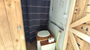 Pieni, käytännöllinen kylpyhuone, jossa on puinen allaskaappi, raidallinen suihkuverho ja wc-istuin.