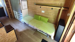 Pieni, kompakti huone, jossa on sänky, puinen seinä, hylly ja jääkaappi.