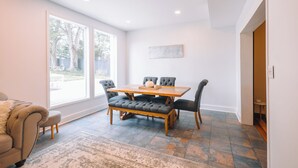 A dining area with a wooden table and four chairs, a bench, and a large window providing a view of the outdoors.