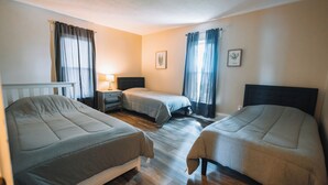 A room with three beds, a nightstand, a lamp, and two framed pictures on the wall.