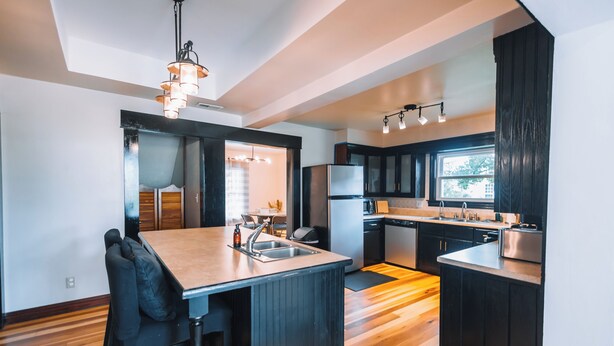 A modern kitchen with a central island, dark cabinetry, and a dining area with a wooden floor.