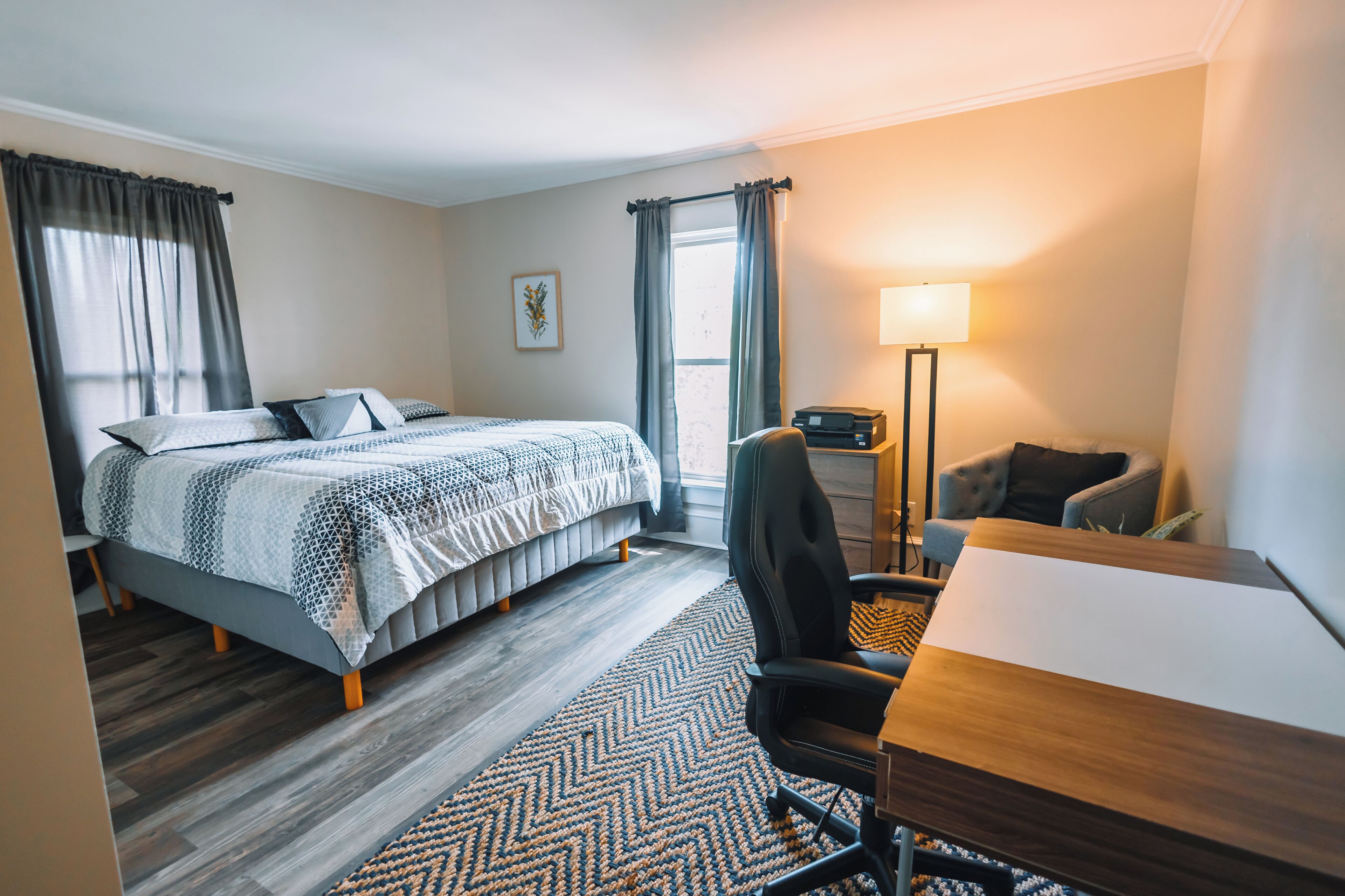 Habitación de hotel con cama, escritorio, silla, lámpara y ventana con cortinas.